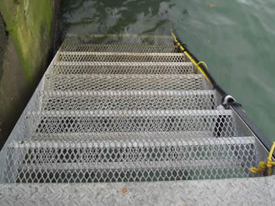 The bottom of a stair made of expanded metal grating connects a river.